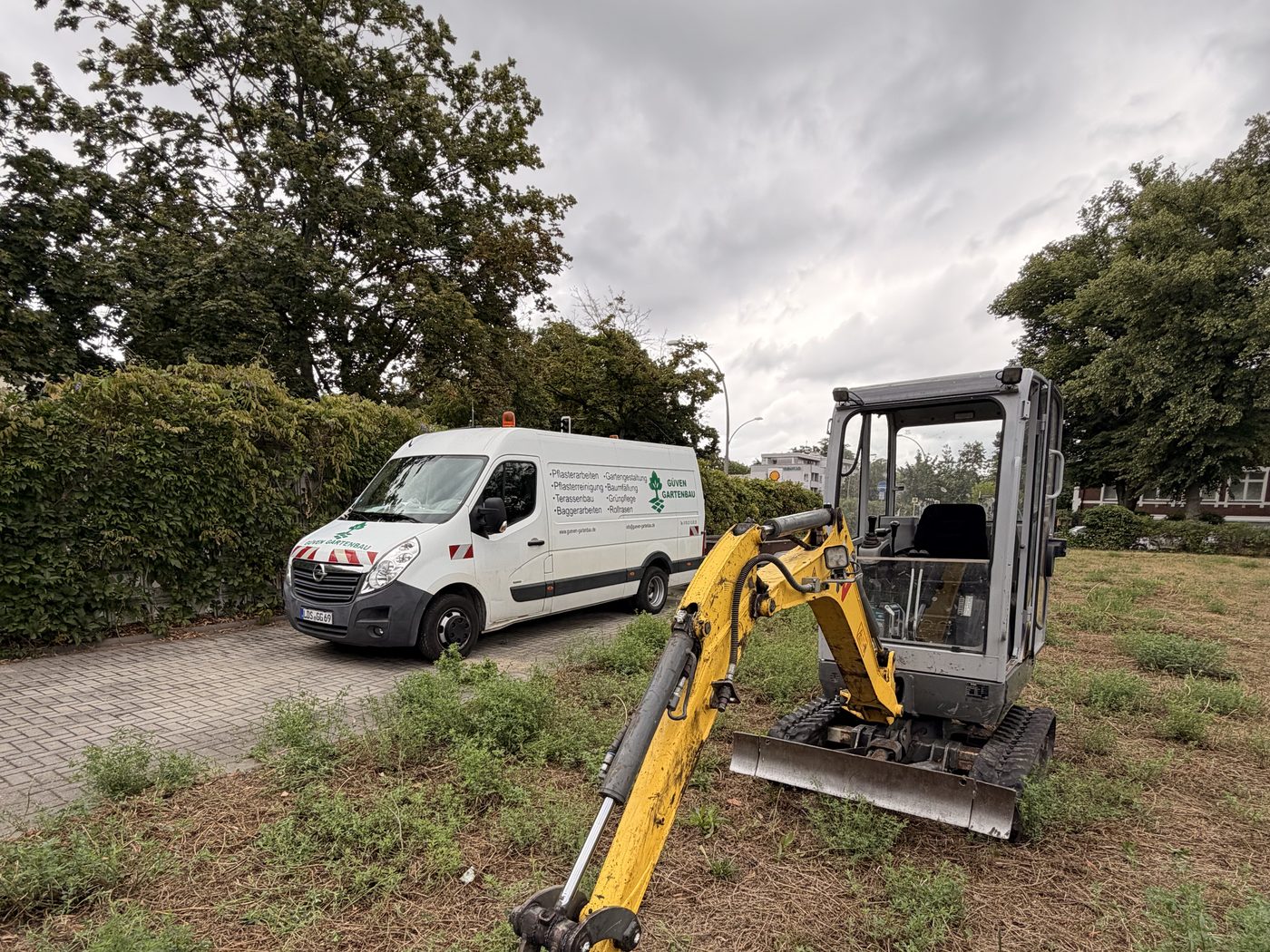 Beschrifteter Transporter und Minibagger von Güven Gartenbau auf einer Baustelle